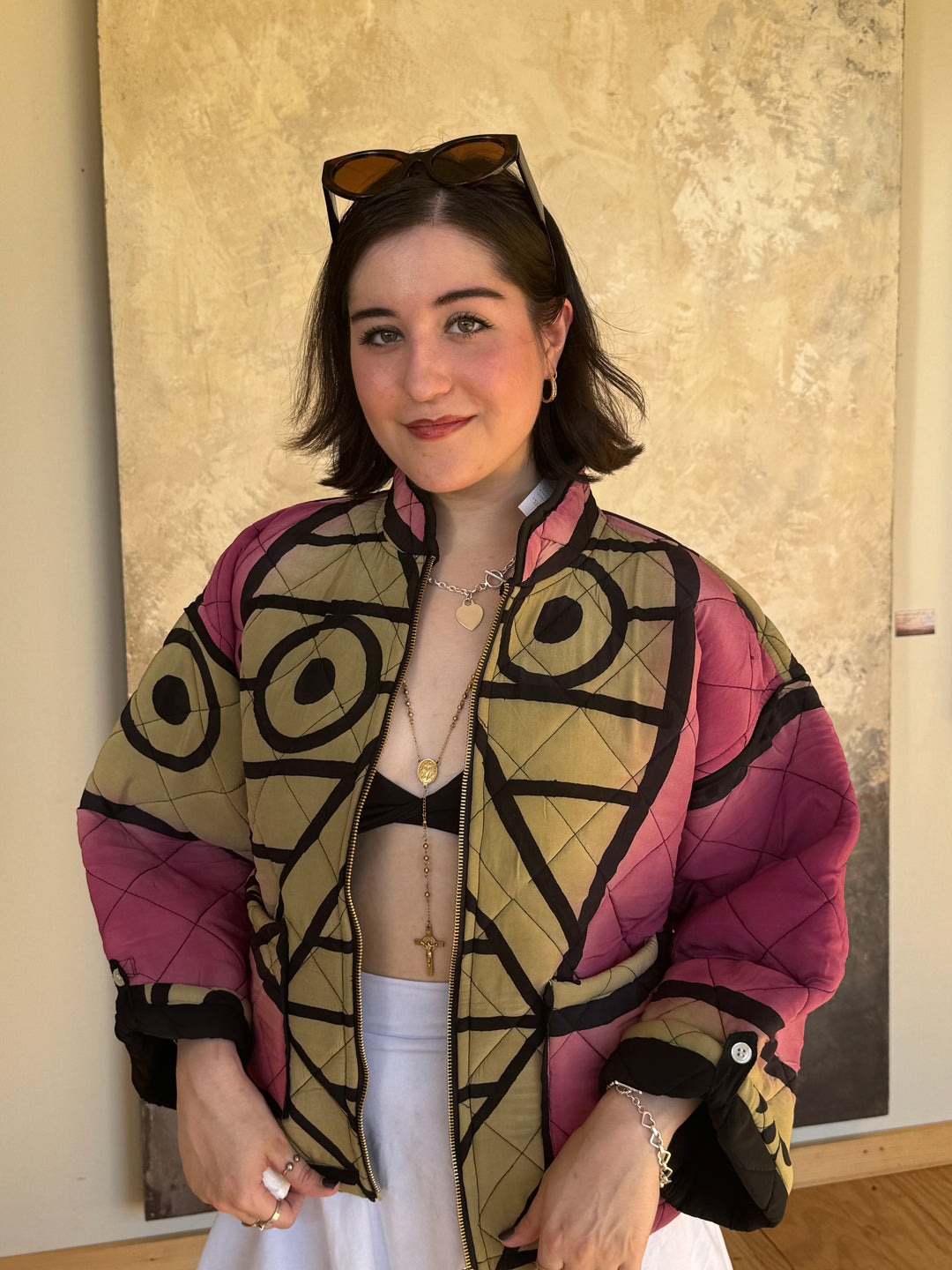 Dark haired model wearing pink and black quilted silk bomber jacket with white skirt