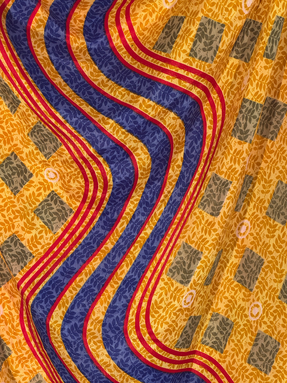 Close-up of a patterned silk blend with wavy blue and red lines on a yellow background.