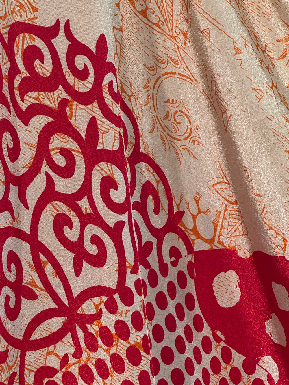 Close-up of patterned silk blend with red and orange designs on a beige background