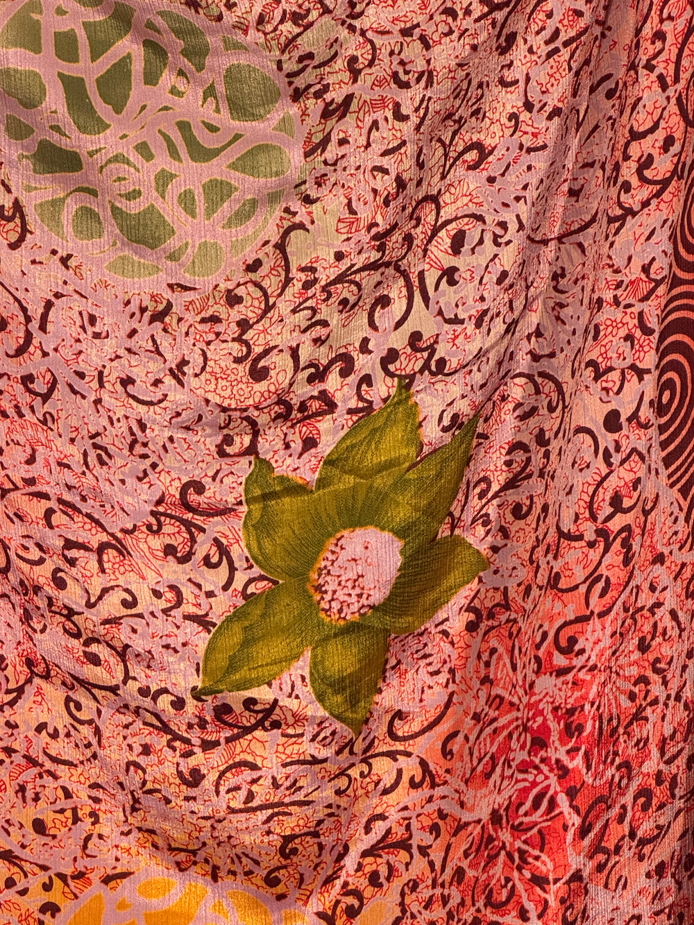 Close-up of a floral silk blend with intricate pink and red patterns and green leaves. 