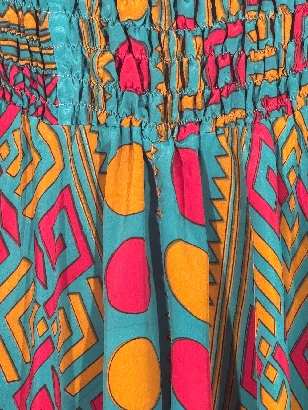 Close-up of colorful upcycled silk blend with geometric pattern on a teal blue/green background
